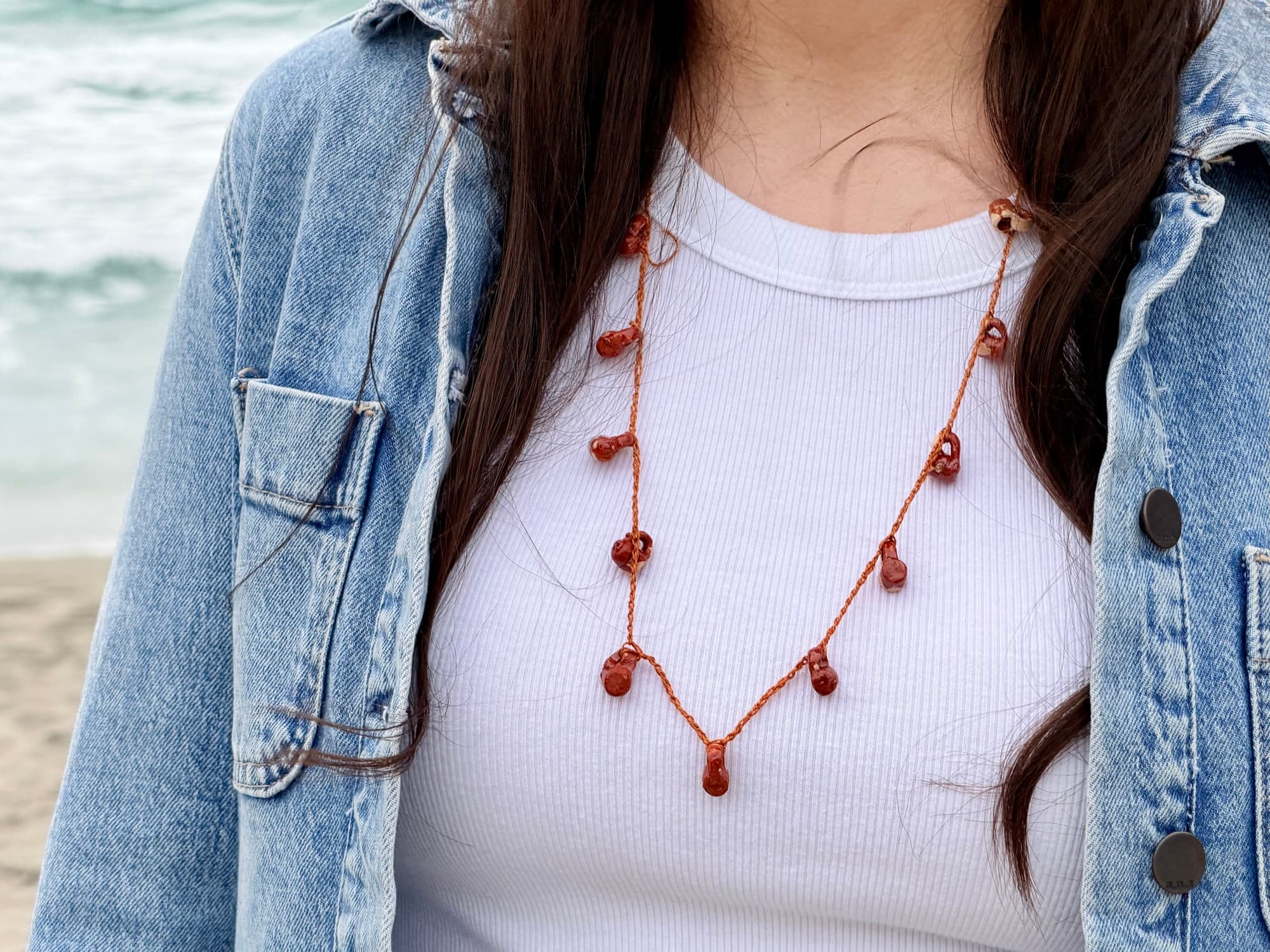 A cinnamon-red jarrito collar worn over a white top by the ocean.