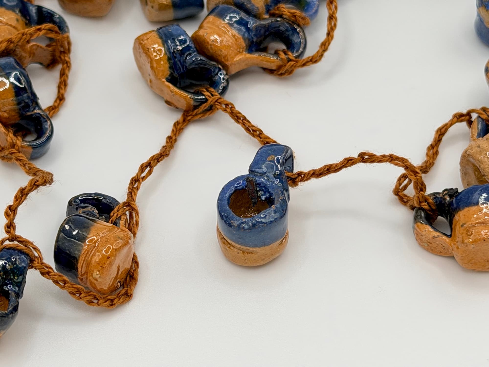 Close-up of Agua del Río jarritos, half deep blue glaze and half bare clay, on a brown cord.