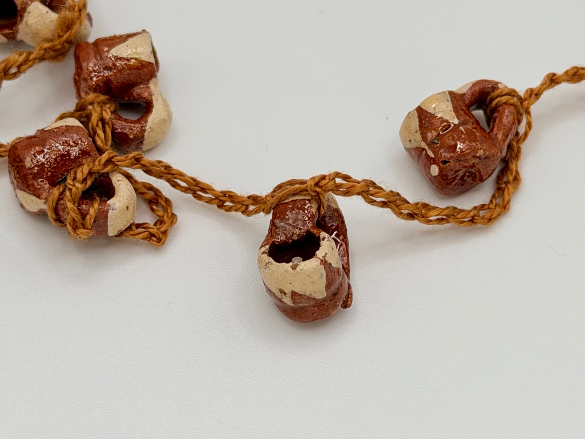 Close-up of Canela y Barro jarritos in reddish-brown clay with cream patches on a tan cord.