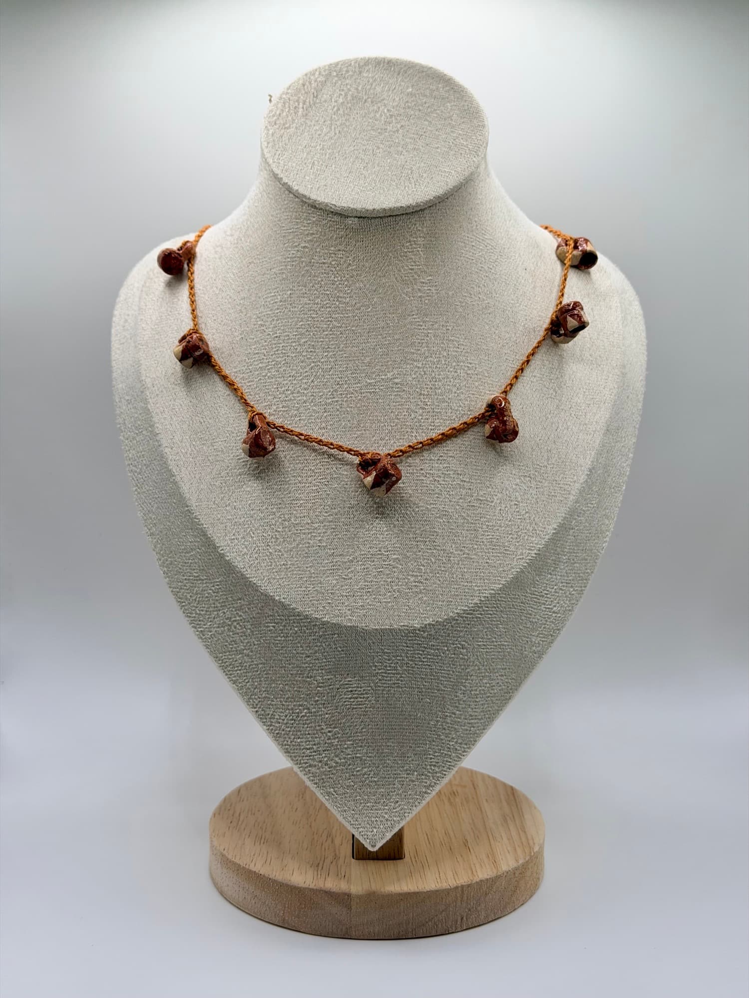 Canela y Barro displayed on a linen necklace bust.