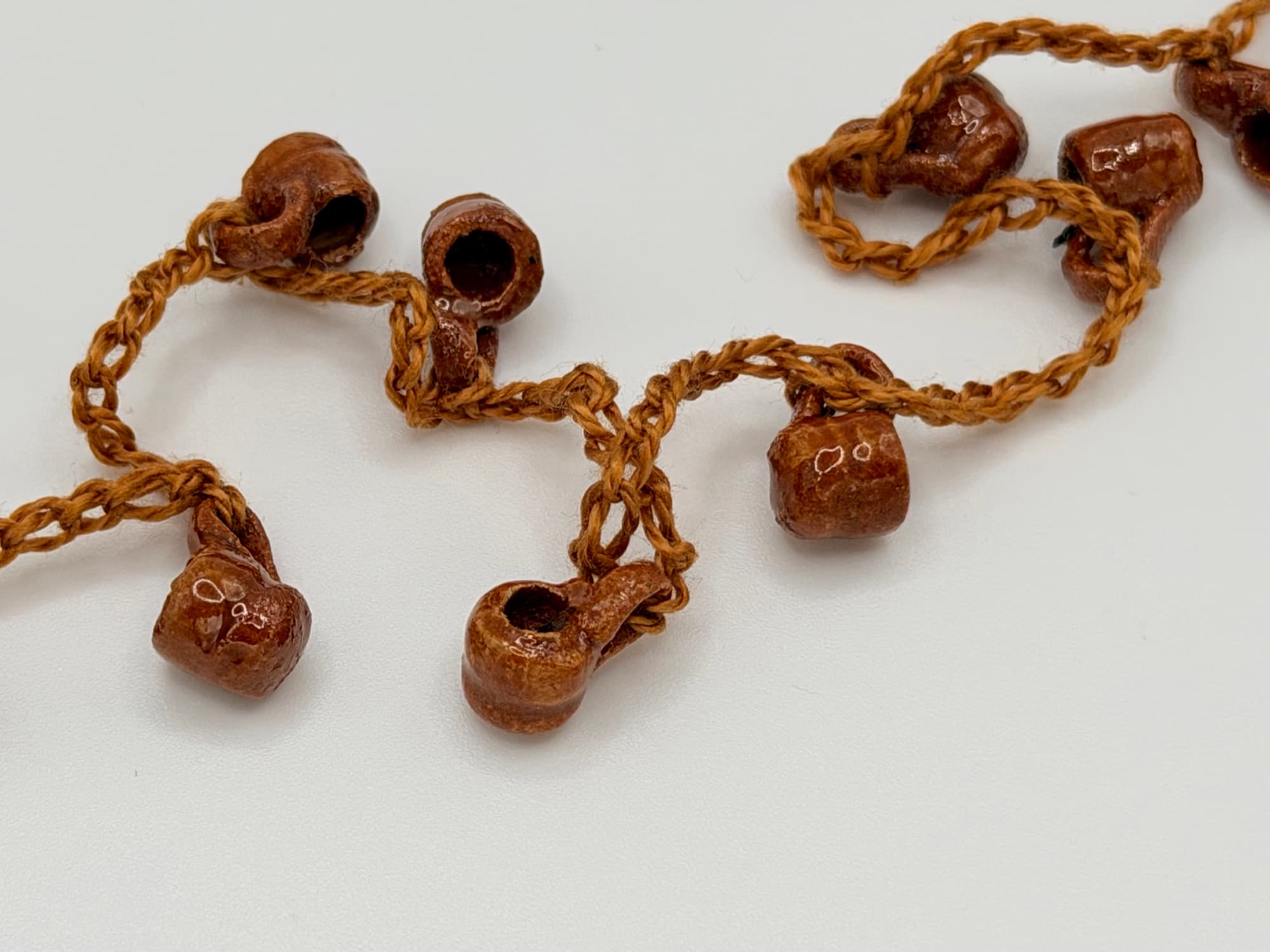 Close-up of Fiesta de Barro jarritos in glossy terracotta on a tan cord.